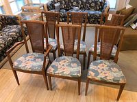 Front view of six wooden dining chairs with cane backs and floral seats