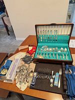 Overall view of open chest with flatware set, loose cutlery and accessories on table