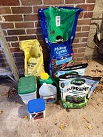 Group shot of potting mix, grass seed, ice melt, vinegar, and assorted lawn care containers against brick wall