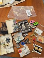 Table view of entire lot showing multiple clip-on earrings, brooches, rings, toy cars and packaging