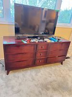 Front view of mahogany dresser under TV showing nine drawers and overall style