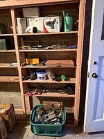 Shelving unit with pot lights, utility pump box, watering can, various hand tools, green tote of hardware