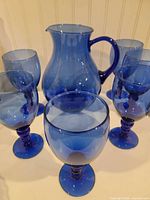 pitcher surrounded by five cobalt blue goblets