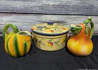 All three ceramic items: lidded crock pot flanked by pumpkin and pear pitchers