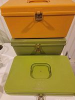 Stacked view showing all three plastic sewing boxes in orange and green with handles and latches