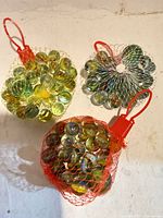 Three mesh bags filled with glass marbles showing colors and packaging