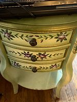 Front view of green floral bombe chest showing three drawers and decorative pulls