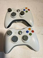 Two white Microsoft Xbox 360 wireless controllers front view showing buttons and joysticks
