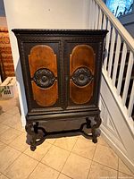 Front view of ebonized Jacobean cabinet showing two doors, carved panels, scrolled base