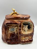 Front view of cookie jar with lid on, showing Barney and Betty relief and bird finial