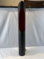 Full view of cylindrical floor lamp showing black exterior and red interior through front cut-out