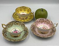 Group shot of three teacup and saucer sets in yellow, green and pink with green apple for scale