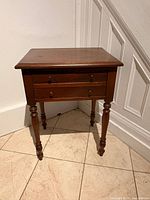 Front view of wooden side table showing top, drawer front, four turned legs