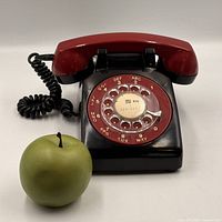 Front view showing black base, red handset, rotary dial, and scale apple