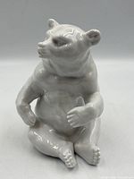 Front-right view of white glazed porcelain bear figurine seated with arms bent and legs forward