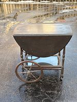 Overall view of walnut drop-leaf tea cart showing one drop leaf down, large spoked wheel, lower glass shelf