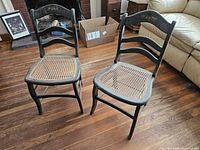 Two black wooden chairs with caned seats on hardwood floor