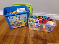 Blue Mega Bloks bin with green lid and clear bin filled with assorted blocks