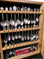 Case open showing three rows of hanging souvenir spoons and boxed spoon at bottom