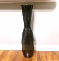 Full view of smoked glass IKEA Fyllig floor vase standing on hardwood floor.