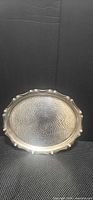 Front view of round silver-tone tray showing textured center and scalloped rim