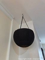 Matte black woven rattan basket hanging from ceiling on chain with hook visible