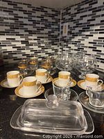 Mixed drinkware showing porcelain cups with gold band, tea glasses, brandy snifters, handled cups, butter dish