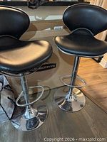 Pair of black faux-leather armless stools on chrome pedestal bases with footrests