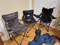 Three folding chairs set up indoors, carry bags on floor