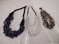 Three necklaces laid out: blue disc bead, silver chains, green stone chips