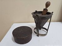 Wood firkin with lid beside metal conical ricer and pestle
