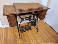 Full view of closed oak cabinet atop black cast iron treadle base