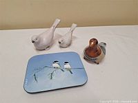 Three ceramic bird figurines and rectangular tin displayed
