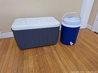 Rectangular cooler and cylindrical thermos side by side on floor
