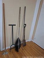 Four long-handle tools and fishing net leaning against wall