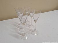 Six clear stemmed glasses on white surface