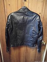 Rear view of black leather motorcycle jacket hanging on wooden door