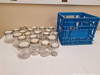 Group of glass canning jars with lids alongside blue plastic crate