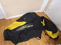 Overall view of black and yellow Ski-Doo snowmobile cover laid out on floor