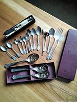 All items laid out on table: boxed knife, loose spoons, meat fork, embossed spoon, boxed set of three serving spoons