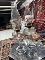 Two clear glass oil lamps side by side showing full height and chimneys