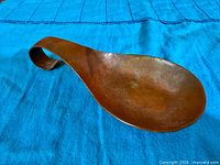 Full view of hammered copper spoon rest on blue cloth