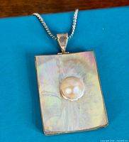 Front view showing rectangular sterling pendant with centred Mabe pearl on blue background