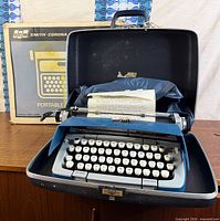 Typewriter seated in open hard case with original cardboard box in background