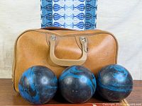 Three candlepin balls in front of tan bag