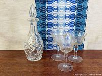 Full view of cut crystal decanter with stopper and four etched glasses on wooden surface