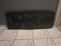 Long black keyboard case leaning against wall showing handles and D-ring