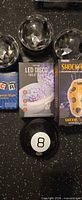 Overview of all items: three crystal dome lights, Traxx LED Disco Toilet Light box, Paladone ShockTato box, Magic 8 Ball, LCR dice game