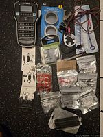 Overview of lot showing label maker, magnetic tins, cables, keychains, phone ring holders and sealed accessory packs