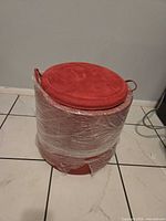 Full view of ottoman wrapped in plastic showing color, shape, and damage at base